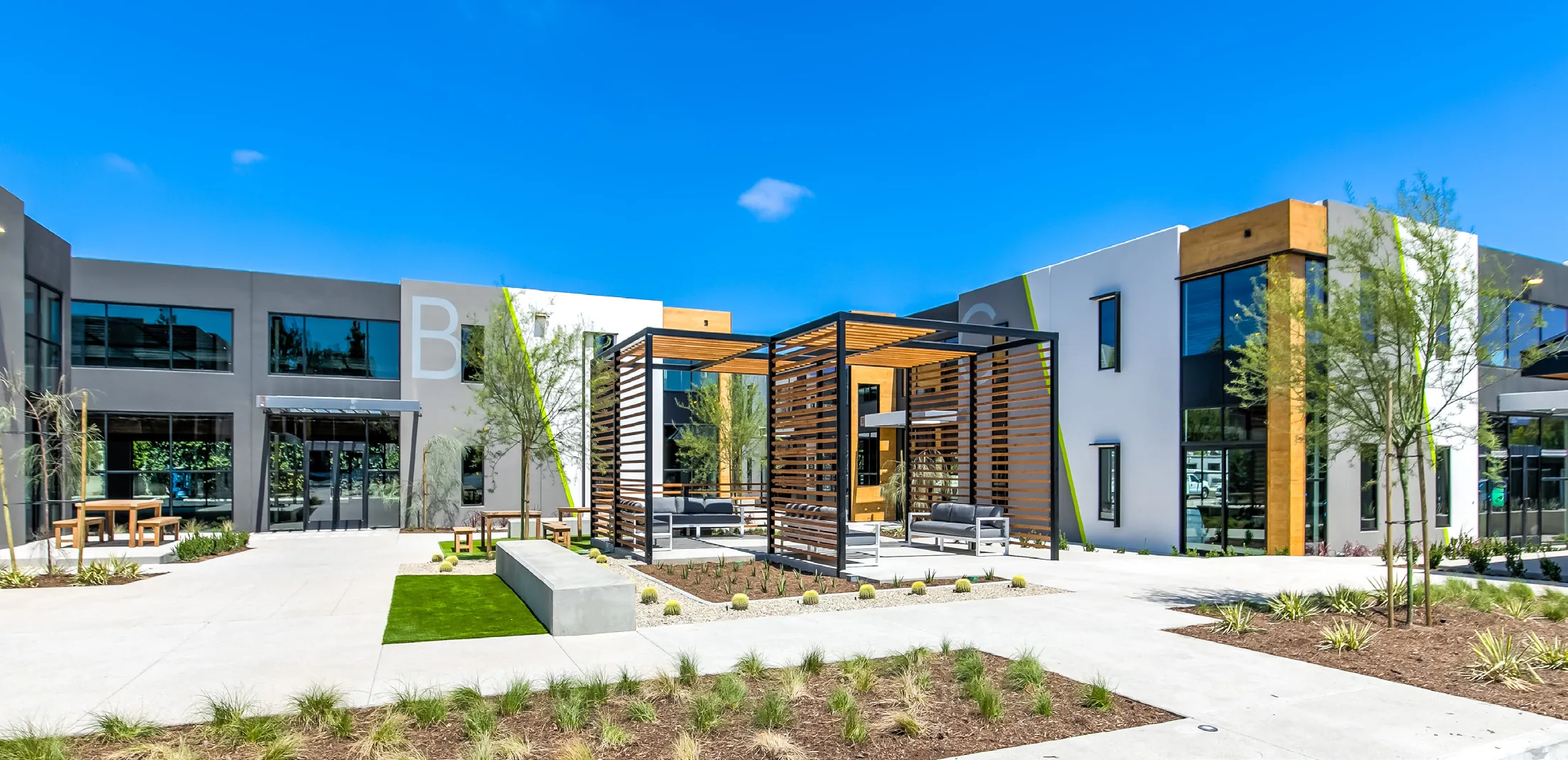 Building B at 660 Baker and its courtyard, with wood pergolas and outdoor tables